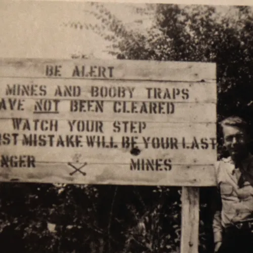 Myron Floren standing next to a minefield warning sign.
